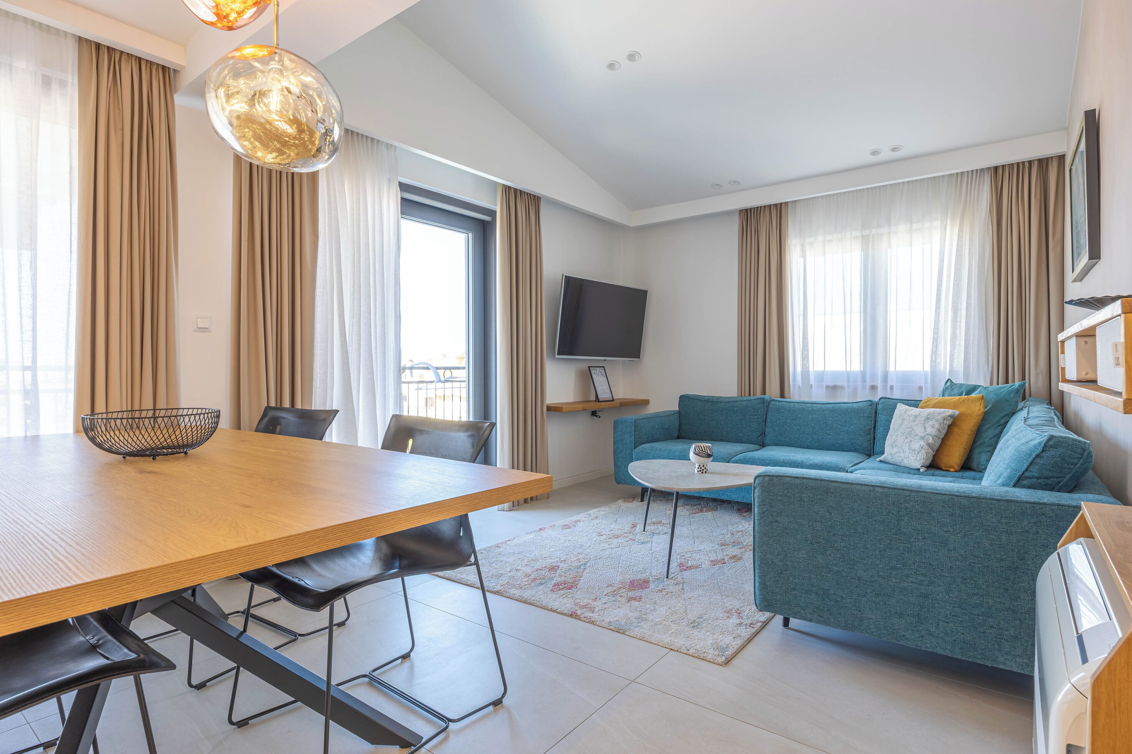 A modern living room with a dining table, sofa, TV, and large windows with curtains.