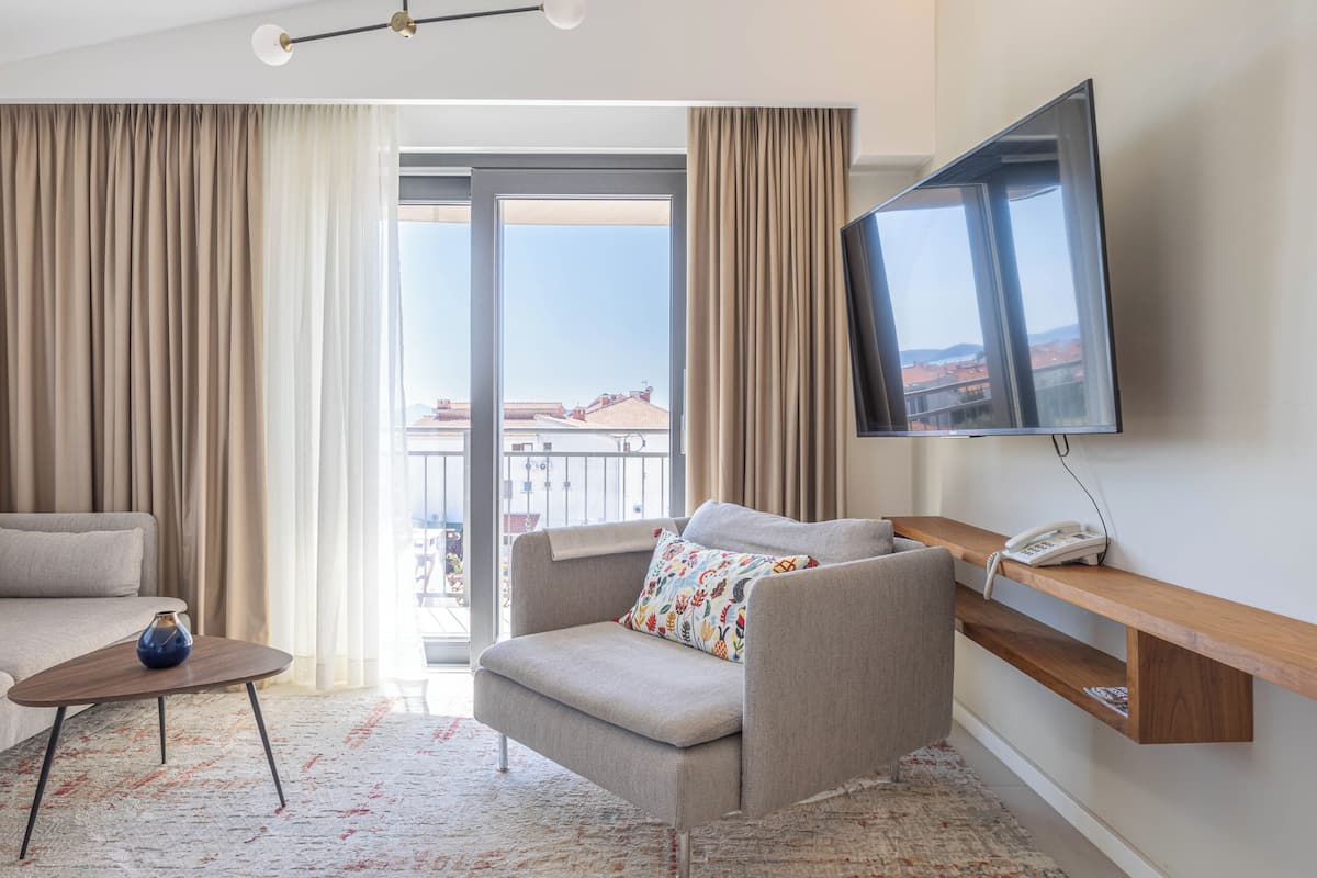 Ein Hotelzimmer mit Sofa, Sessel, Fernseher und einem Balkon mit Blick.