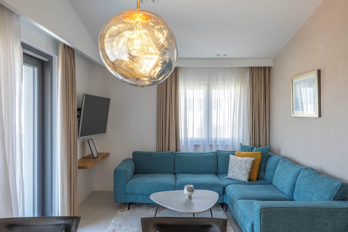 Ein modernes Wohnzimmer mit einer Eckcouch, einem Couchtisch, einem Fernsehgerät auf einem Schrank und einer großen Pendelleuchte.