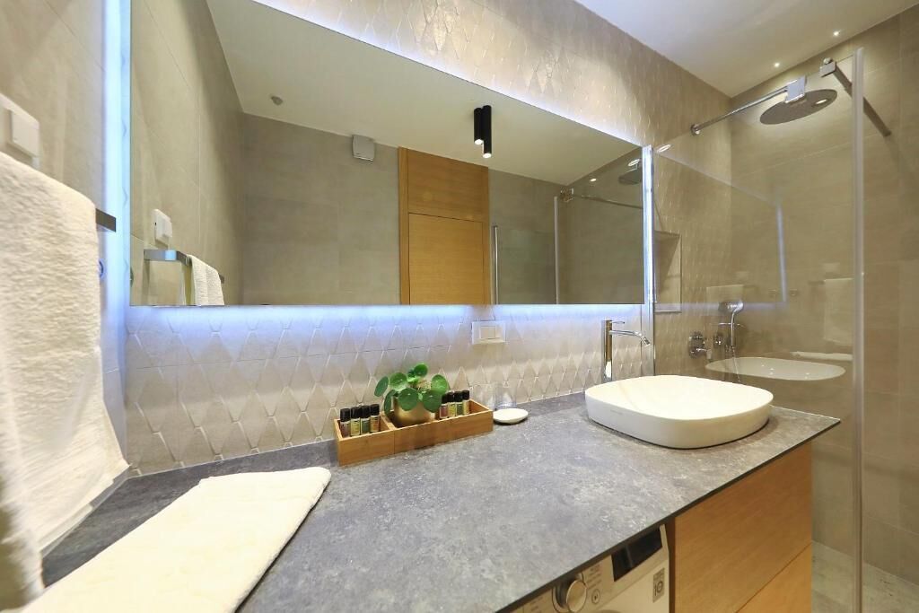 A modern bathroom with a large mirror, a round sink, and a shower.