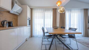 A modern kitchen with white cabinets, a wooden countertop, a dining table with chairs, and a pendant light.