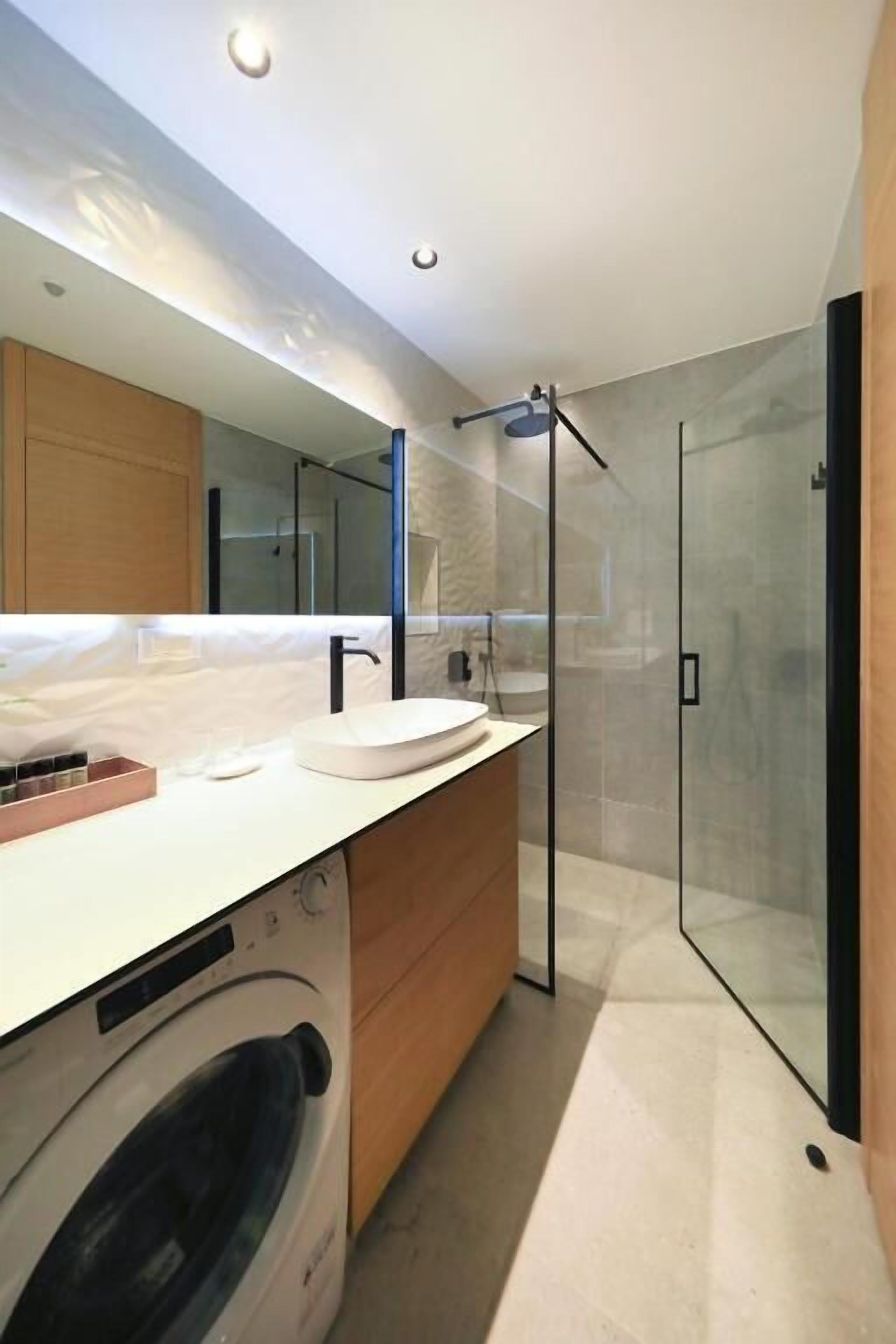 A modern bathroom with a glass shower enclosure, a built-in washing machine, and a large mirror.