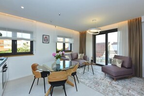 A modern living room with a glass dining table, a sofa, and a balcony with a view.