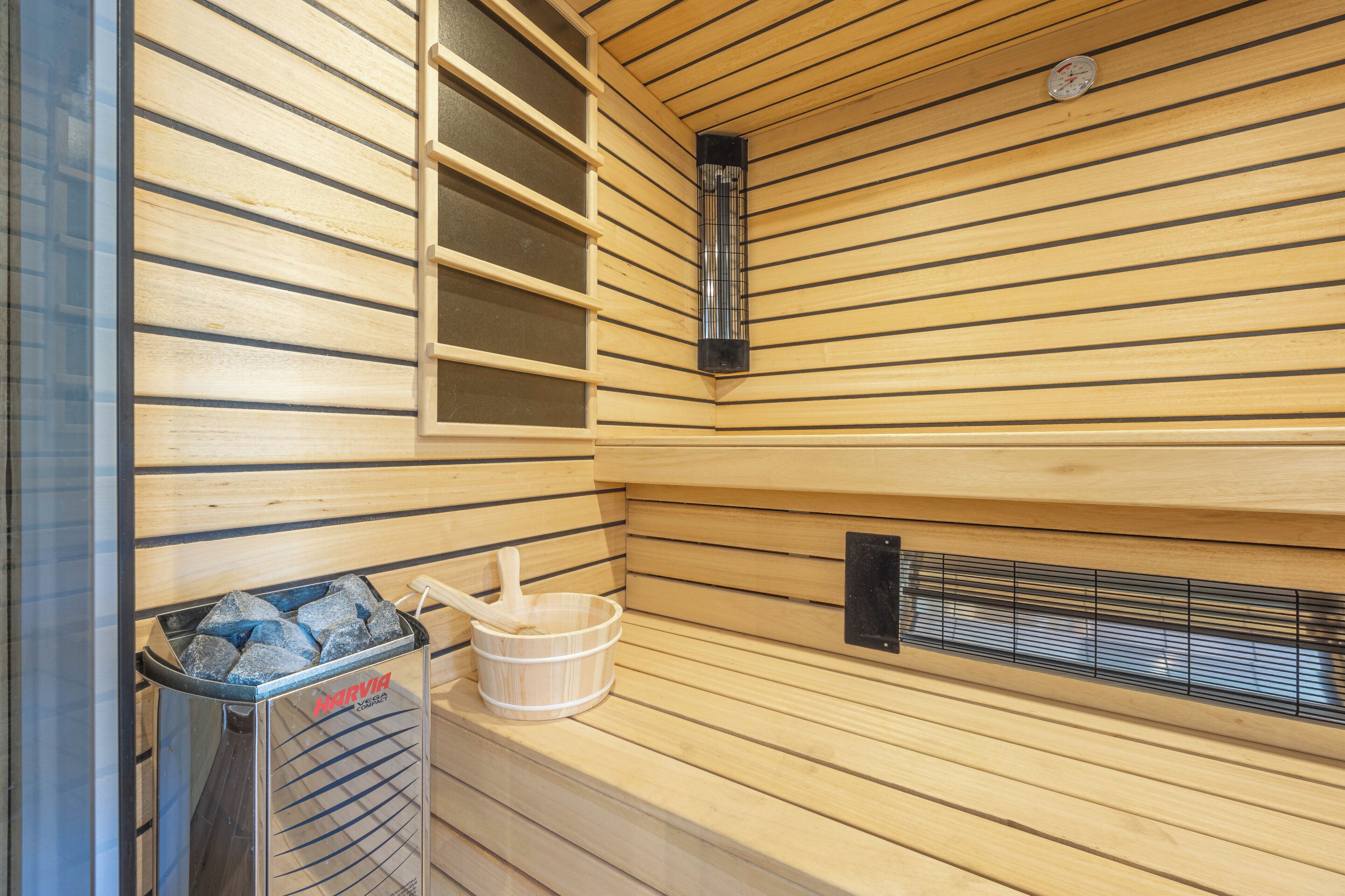 A sauna with wooden walls, a heater, a bucket with a brush, and a trash bin.