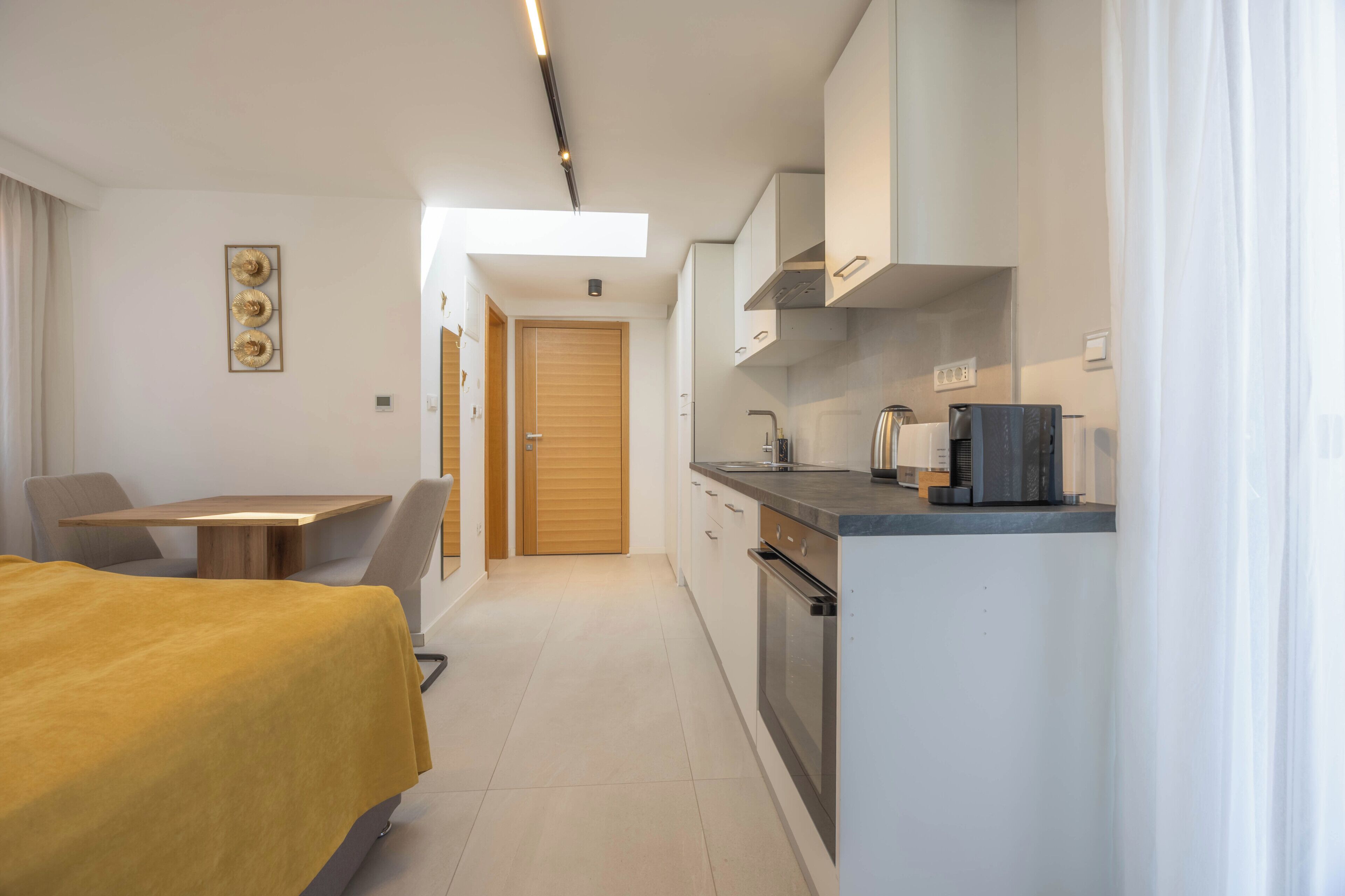 Een kleine hotelkamer met een bed, een tafeltje, een kitchenette en een houten deur.