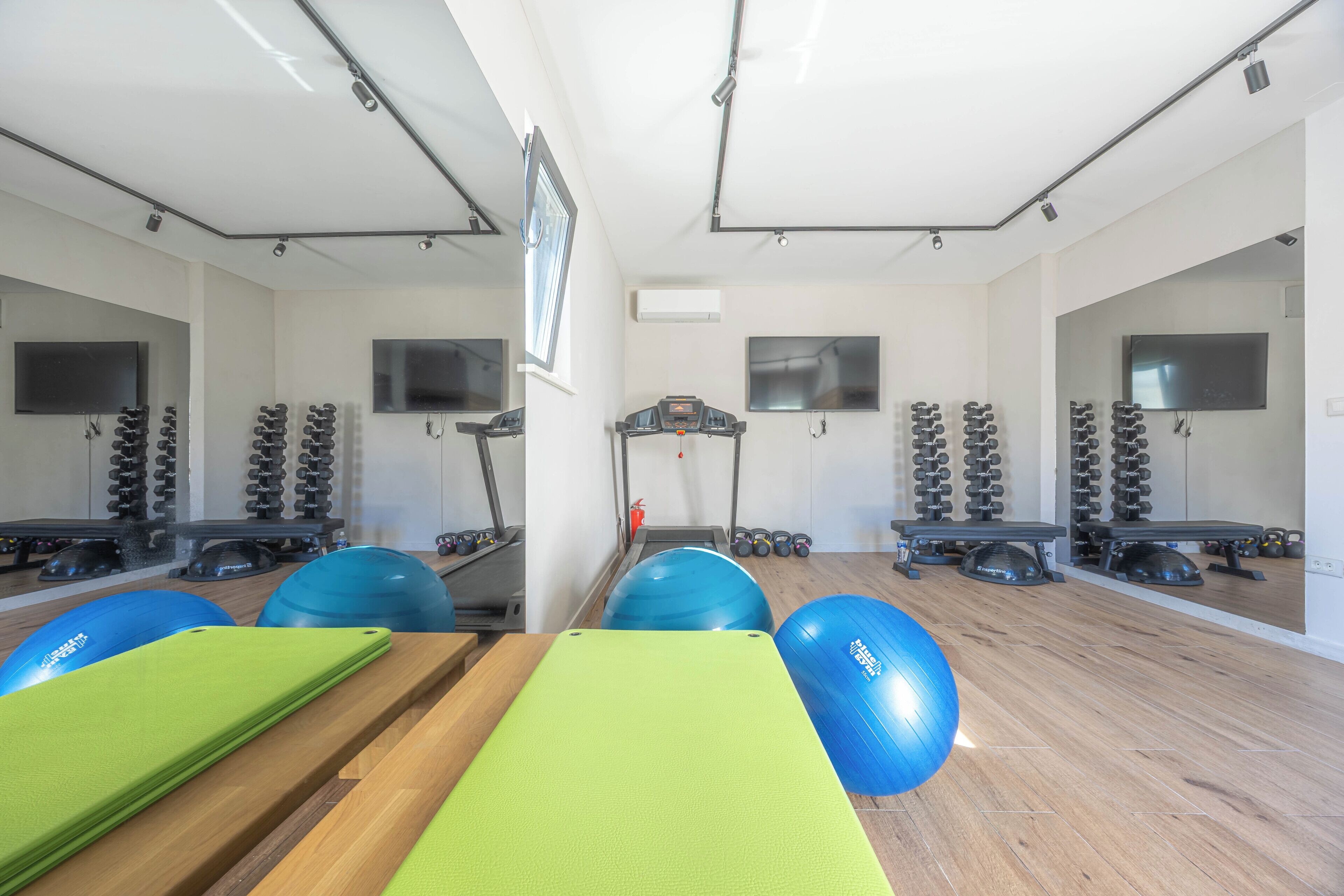 A gym with exercise equipment, mirrors, and a wooden floor.