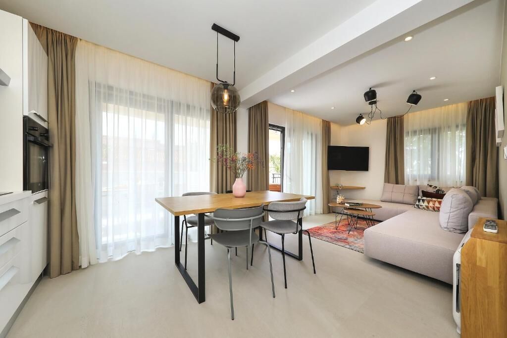 Een moderne woonkamer met een bank, televisie, eettafel, stoelen en een keuken met inbouwapparatuur.