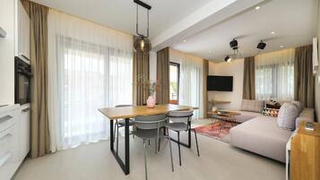 Een moderne woonkamer met een bank, televisie, eettafel, stoelen en een keuken met inbouwapparatuur.