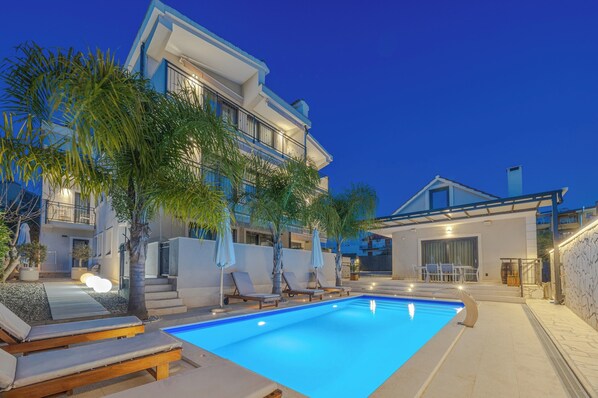 A modern two-story house with a swimming pool, outdoor seating, and palm trees.