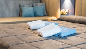 A neatly made bed with rolled towels, a headboard, and a bedside table with a lamp and flowers. - FRUIT VILLAGE PAESTUM Coral Beach (Capaccio-Paestum)