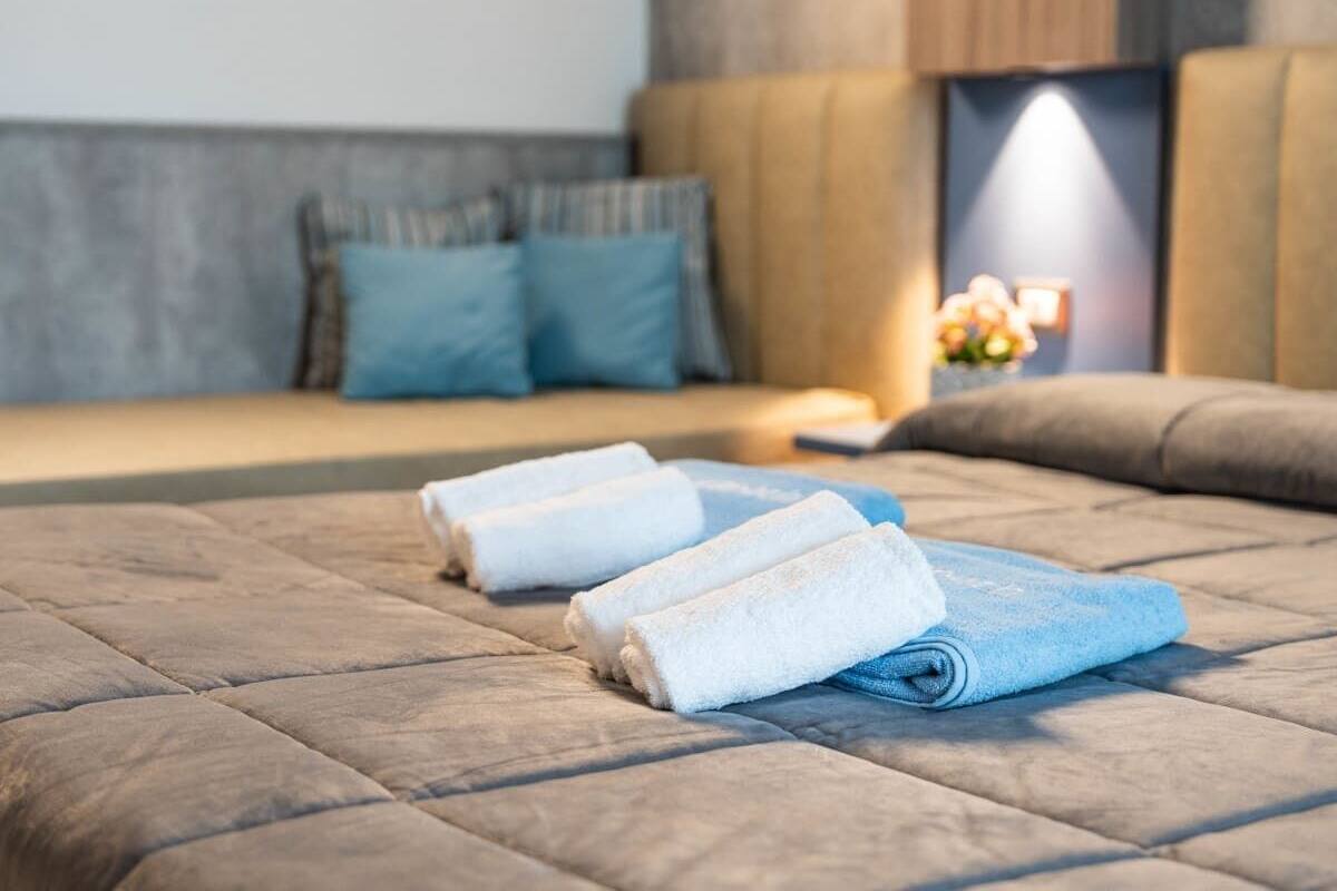 A neatly made bed with rolled towels, a headboard, and a bedside table with a lamp and flowers.
