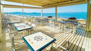 An outdoor deck with tables and chairs, overlooking a beach and ocean. - FRUIT VILLAGE PAESTUM Coral Beach (Capaccio-Paestum)