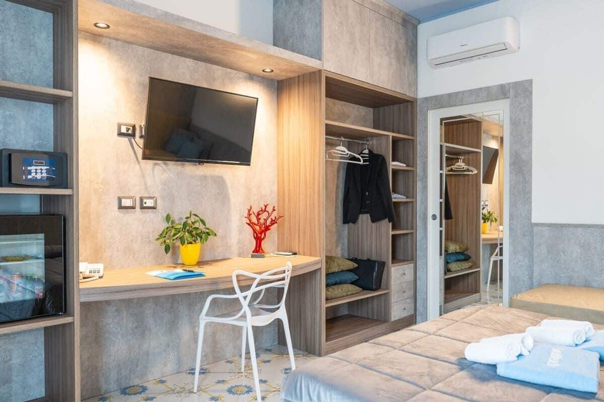 A modern bedroom with a bed, desk, chair, TV, wardrobe, and a small seating area.