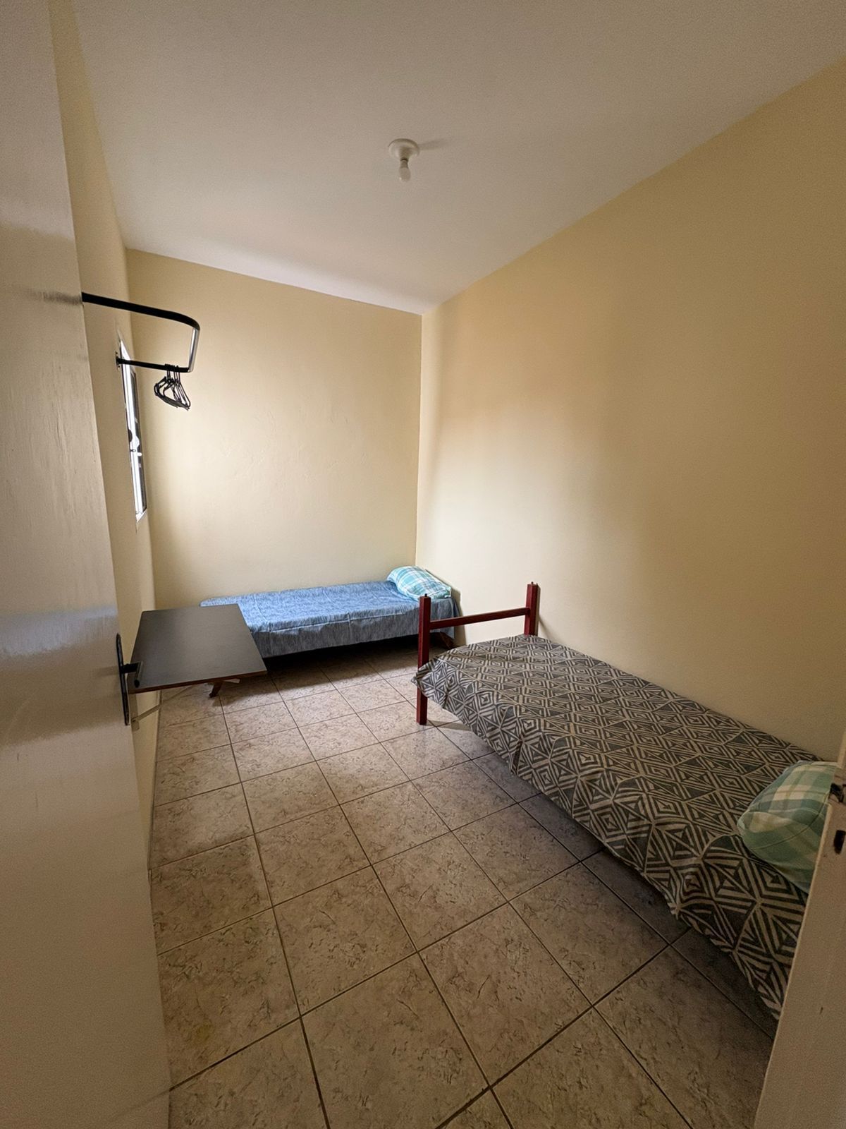 Eine kleine Einzimmerwohnung mit zwei Betten, Fliesenboden und einer Deckenleuchte.