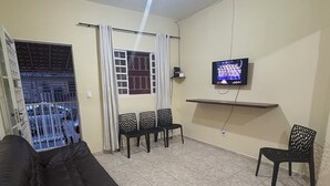 Ein Wohnzimmer mit schwarzem Sofa, einem an der Wand montierten Fernseher und einem Balkon mit Blick auf die Straße.