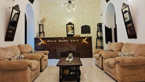 A living room with two sofas, a coffee table, a ceiling fan, and a reception desk with a sign. - Cara Galle Fort (Galle)