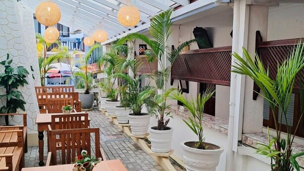 A covered outdoor seating area with wooden tables and chairs, potted plants, and hanging spherical light fixtures. - Cara Galle Fort (Galle)