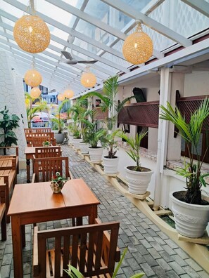 A covered outdoor seating area with wooden tables and chairs, potted plants, and hanging spherical light fixtures. - Cara Galle Fort (Galle)