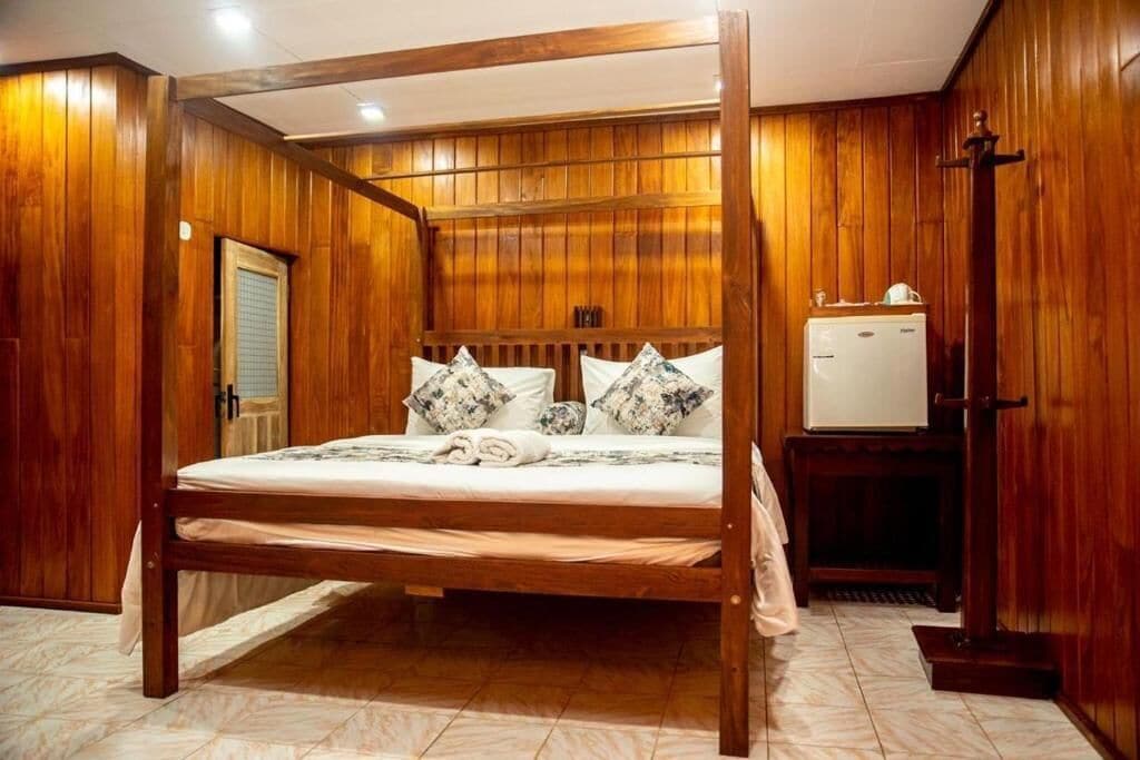 Un lit à baldaquin en bois, doté d’un matelas blanc et d’oreillers à motifs, une petite table de chevet et un radiateur intégré.