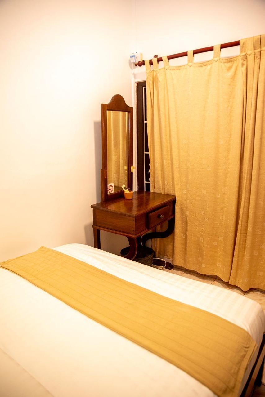 A bedroom with a bed, a wooden nightstand, a mirror, and a curtain.