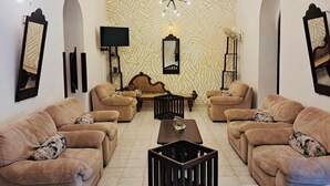 A living room with beige sofas, a wooden coffee table, a TV, and a patterned wall. - Cara Galle Fort (Galle)