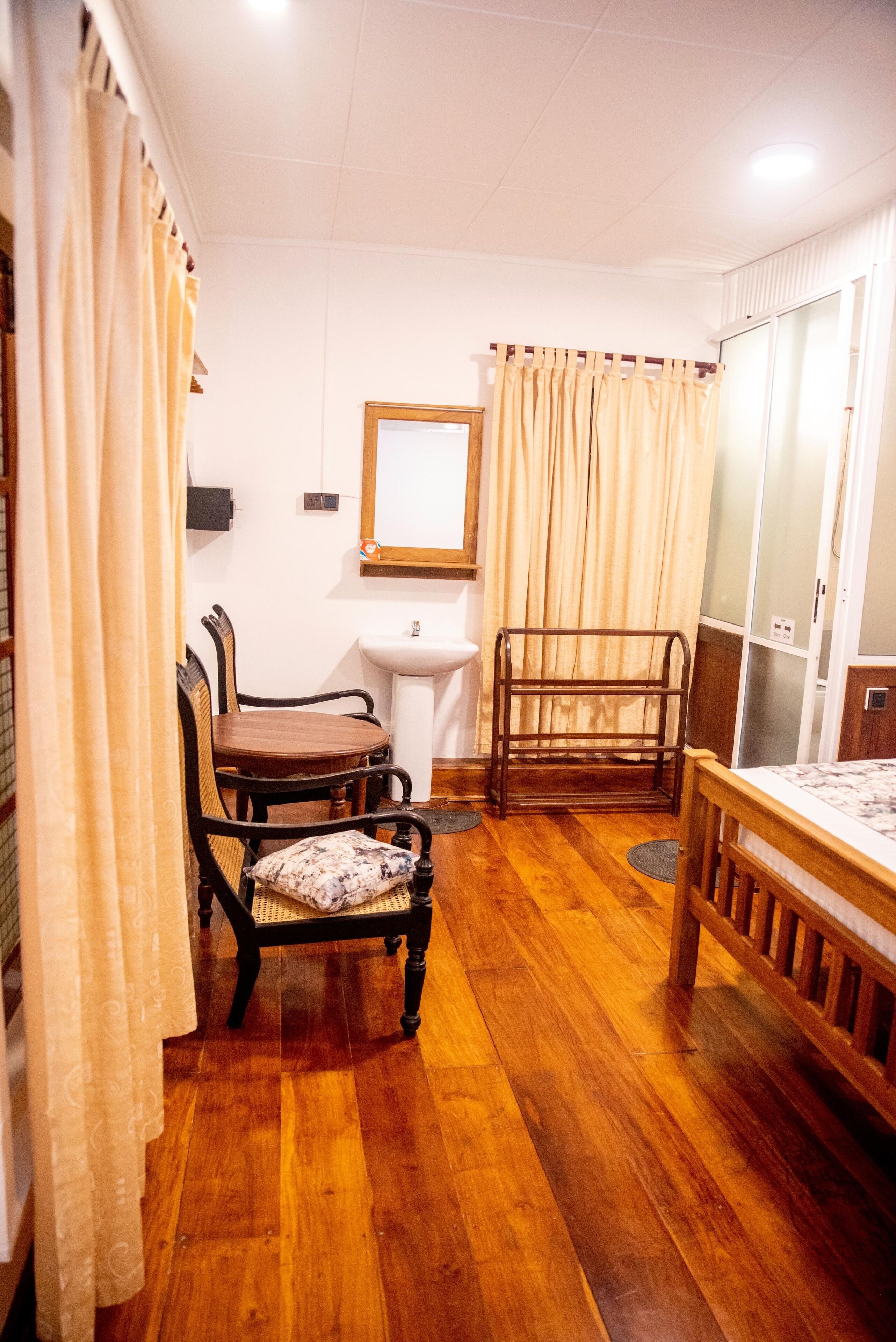 A room with wooden flooring, a dining table with chairs, a bed, a sink, and curtains.