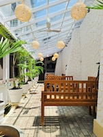 A covered outdoor area with wooden benches, potted plants, and hanging light fixtures.