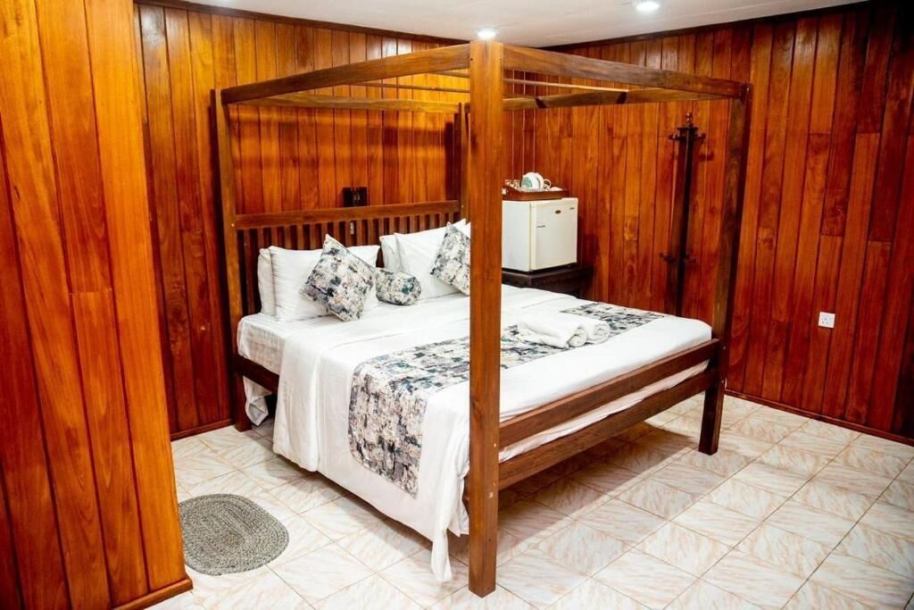 A wooden four-poster bed with a white bedspread and pillows, a small bedside table, and a nightstand.