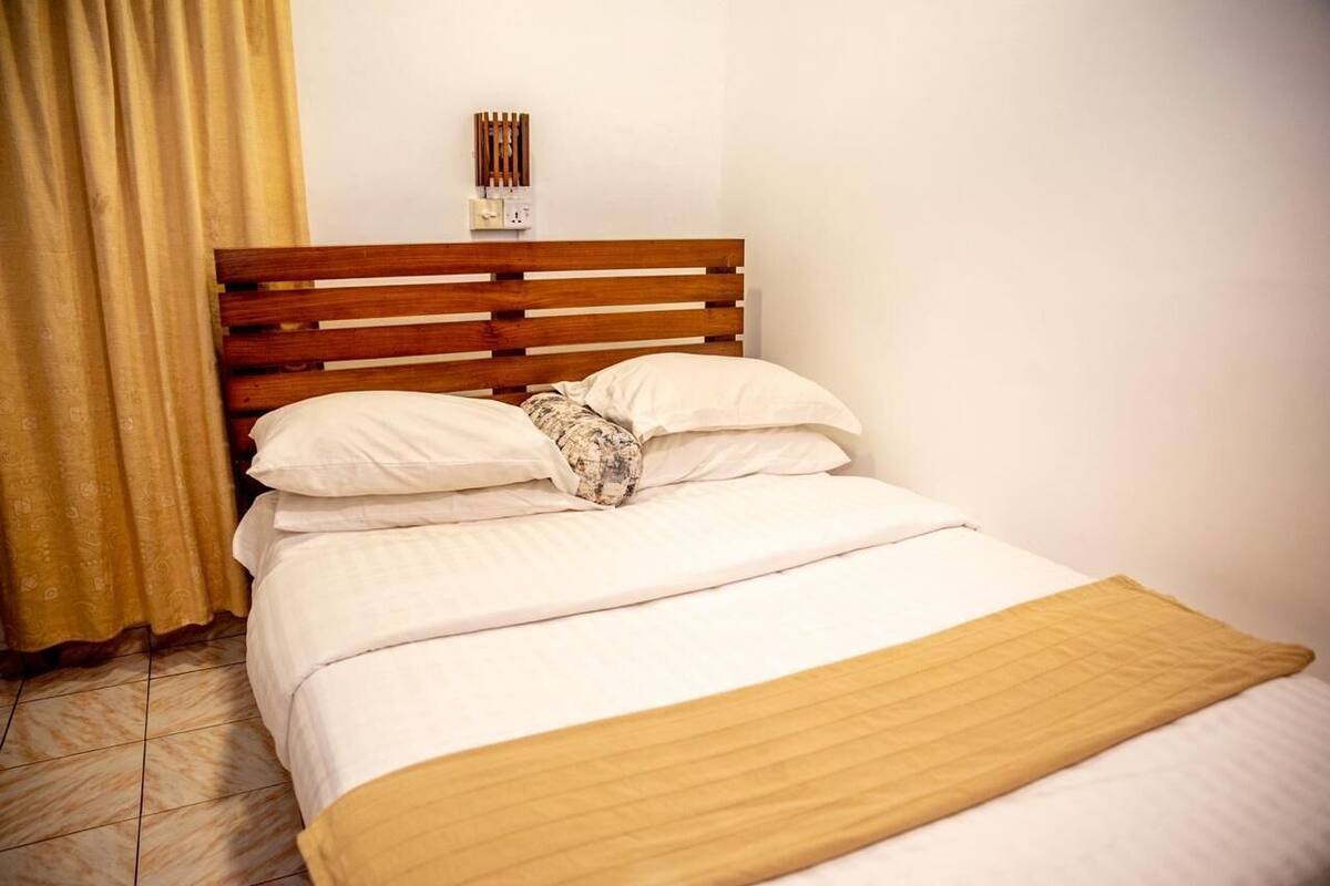 Una cama bien hecha con cabecera de madera, una colcha color beige y un cojín estampado.