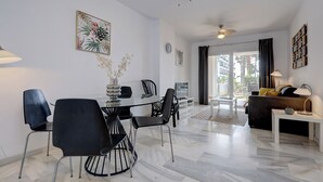 Moderni olohuone, jossa on ruokailutila. Tilaan kuuluu lasipöytä, mustat tuolit, sohva ja kattotuuletin.