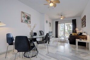 A modern living room with a dining area, featuring a glass table, black chairs, a sofa, and a ceiling fan. - Ground floor 2 bd, 2 bth apt, beachfront complex in Calahonda, Mijas (Mijas)