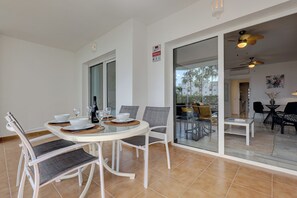A dining area with a round table, white chairs, and a bottle of champagne. There is a sliding glass door leading to an outdoor seating area. - Ground floor 2 bd, 2 bth apt, beachfront complex in Calahonda, Mijas (Mijas)