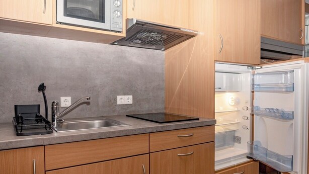 A compact kitchen with a built-in microwave, a stainless steel sink, and a refrigerator with clear storage bins. - Enjoyable 1-bedroom apartment in beautiful Stuttgart city center W1_P13 (Stuttgart)