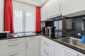 Una cocina moderna con armarios blancos, encimera negra y cortinas rojas.