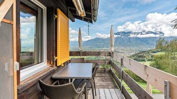 A wooden deck with a table and chairs, overlooking a mountainous landscape.