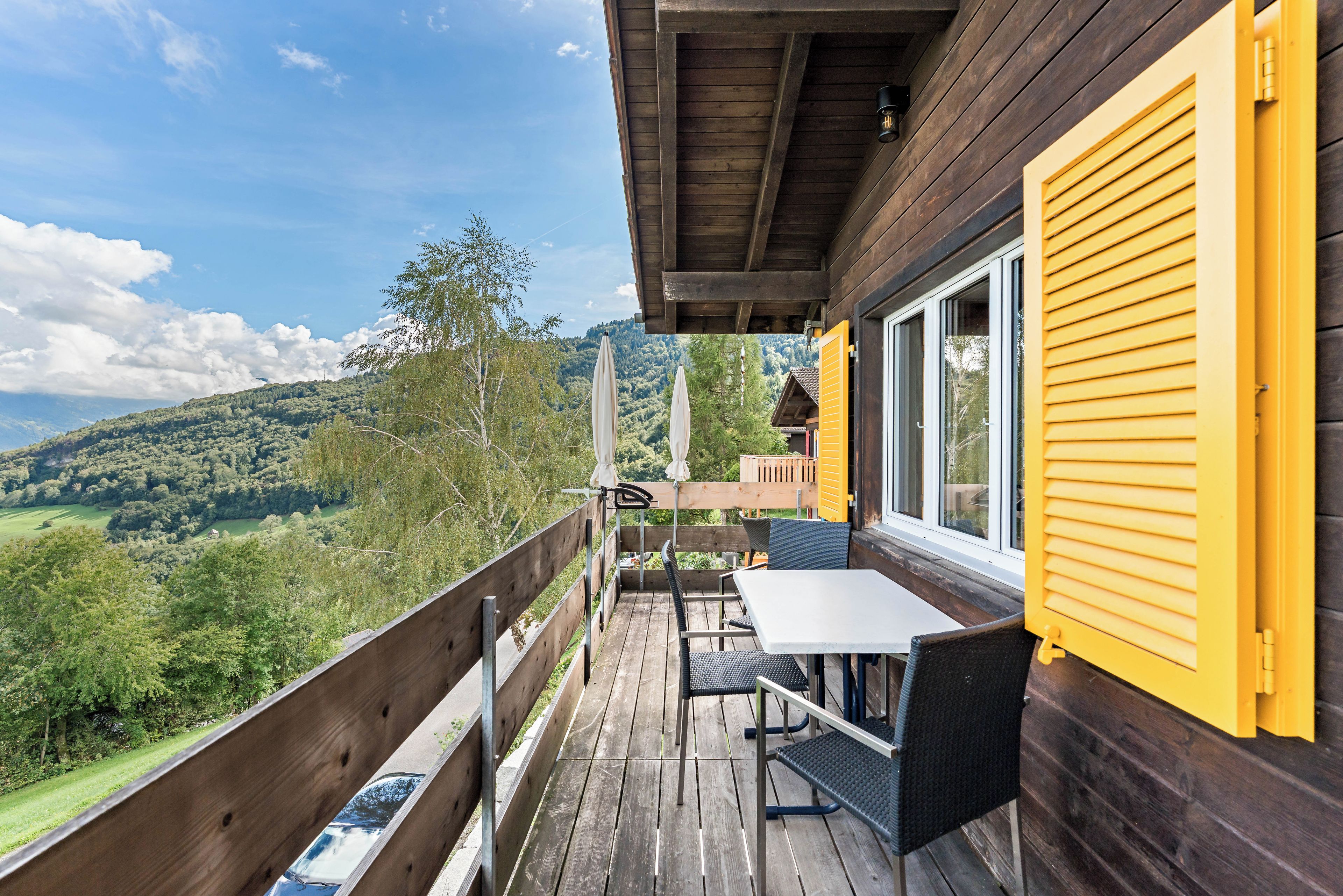 Una terraza de madera con una mesa y sillas, con vistas a un paisaje verde.