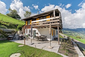 Ein zweistöckiges Holzhaus mit Balkon, Sitzgelegenheit im Freien und Blick ins Grüne.