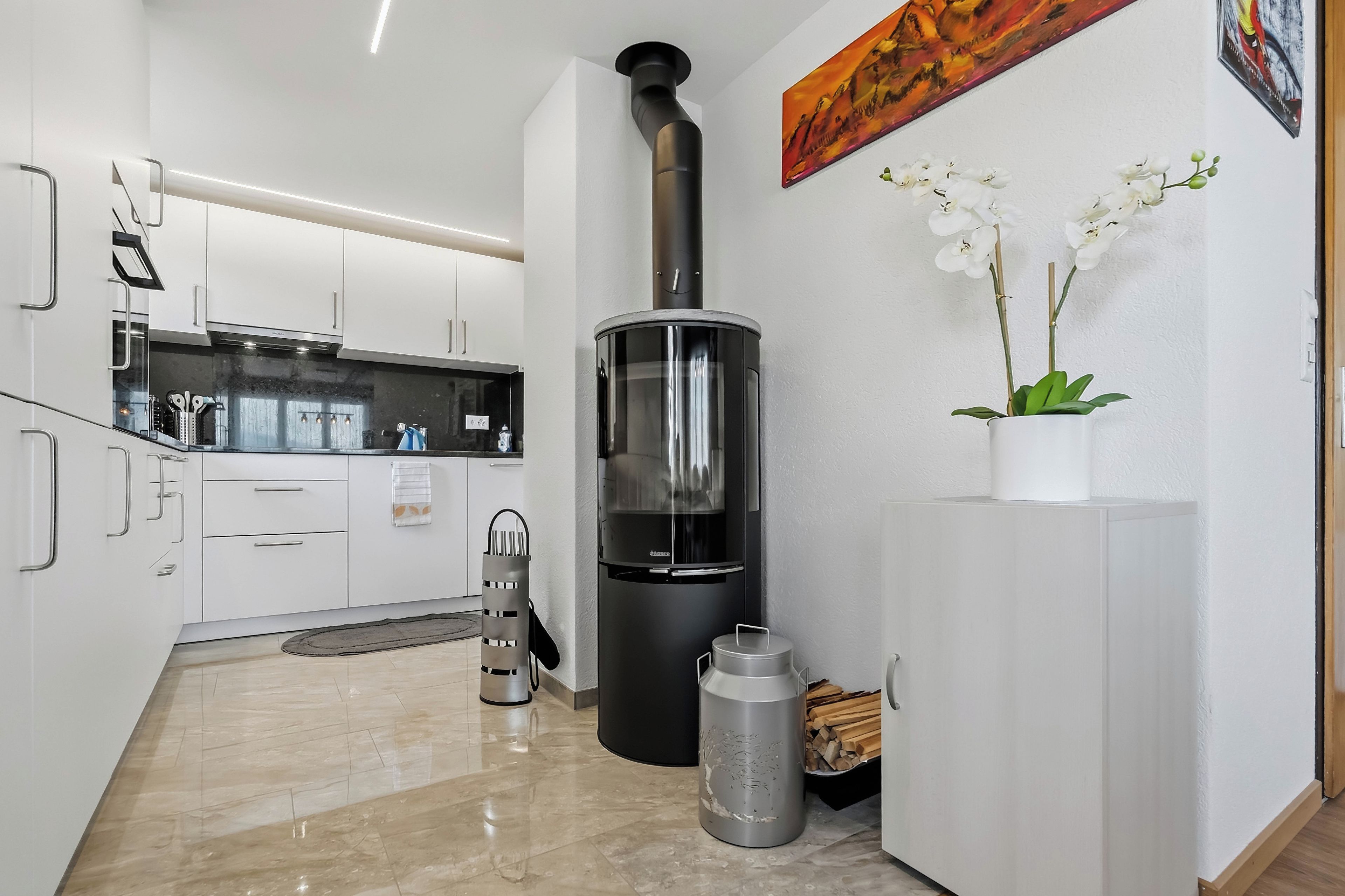 A modern kitchen with white cabinets, a black stove, and a small potted orchid on the counter.