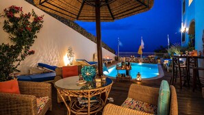 A poolside area with wicker furniture, a table with a decorative vase, and a pool with a fence. - Castri Village Kythira - Phoenix Sea View Retreat (Kithira)