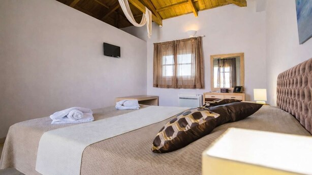 A bedroom with a bed, a bedside table, a mirror, and a window with curtains. - Castri Village Kythira - Andromeda Sea View Escape (Kithira)