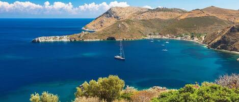 A coastal landscape with clear blue waters, a small island, and a sailboat.