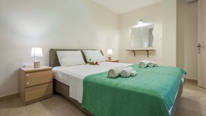 Un lit bien fait, recouvert d’une couverture verte, avec deux lampes de chevet, une table de chevet avec une lampe et un miroir au-dessus du lit.