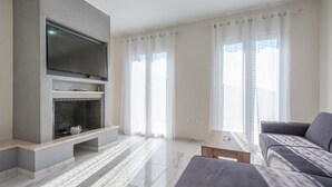 Un salon moderne avec un téléviseur à écran plat fixé sur un mur gris, une cheminée avec un manteau en faïence, un canapé gris et une table basse en bois.