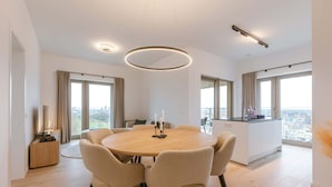 Ein moderner Essbereich mit einem runden Tisch, sechs Stühlen und Blick auf die Stadt durch große Fenster.