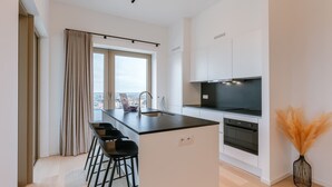 Eine moderne Küche mit Kochinsel, Barhocker, Backofen und großem Fenster mit Aussicht.