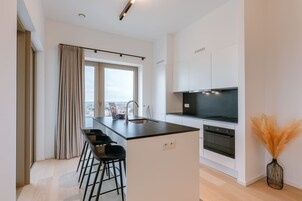 A modern kitchen with a central island, bar stools, a built-in oven, and a large window with a view.