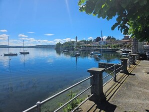 A calm lake with boats, a stone railing, and buildings in the background. - Lake View (Meina)
