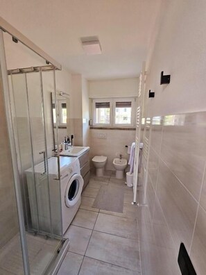 Un baño pequeño con cabina de ducha de vidrio, lavadora, inodoro y bidé.