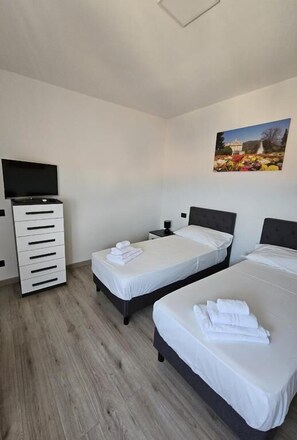 Una habitación de hotel con dos camas individuales, un televisor, un aparador y un cuadro en la pared.