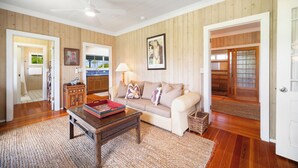 A living room with a sofa, coffee table, and a ceiling fan. There is a wooden floor and a door leading to another room. - Umetsu, Hanalei's Timeless Charm w/ AC TVNC#5096 (Hanalei)